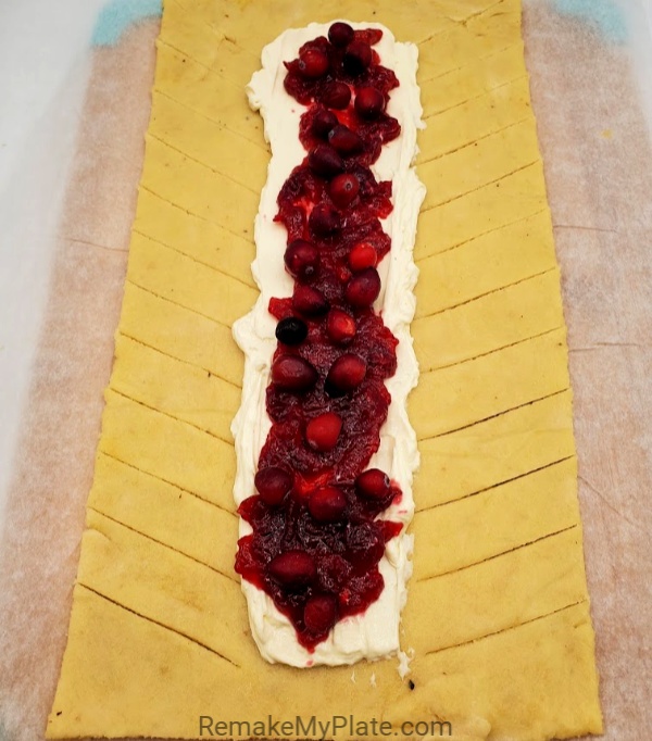 topping the cream cheese mixture with cranberry sauce and whole fresh cranberries
