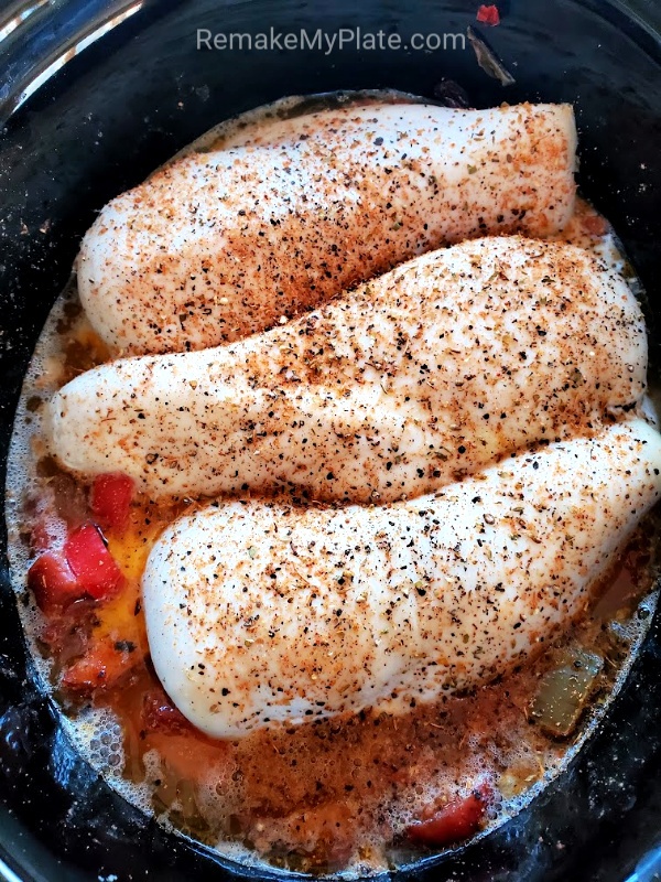 chicken breasts placed on top of other ingredients in the crockpot