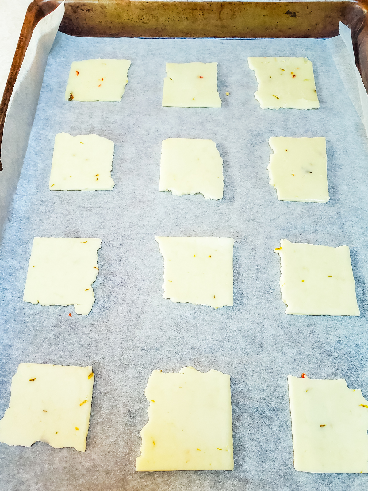 placing pieces of sliced cheese on a baking sheet lined with parchment paper.