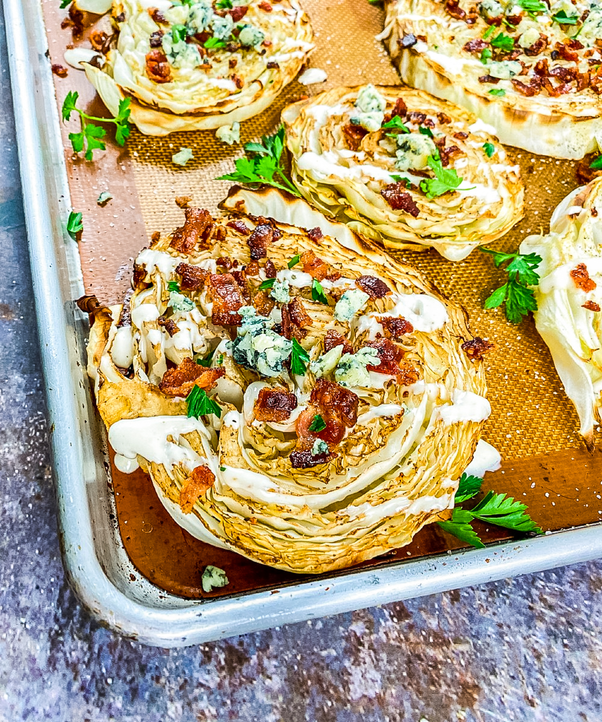 roasted cabbage steaks with blue cheese dressing drizzled over the top sprinkled with bacon