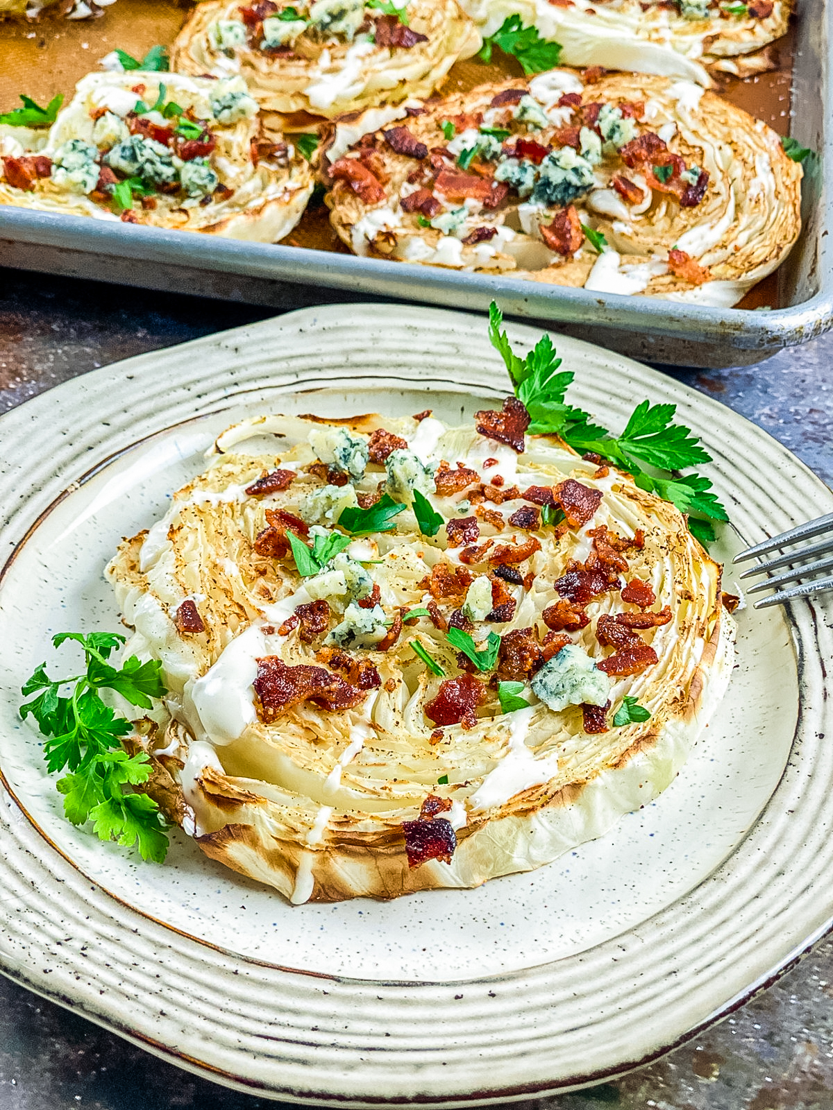 loaded roasted cabbage steaks on a plate topped with blue cheese dressing and bacon bits