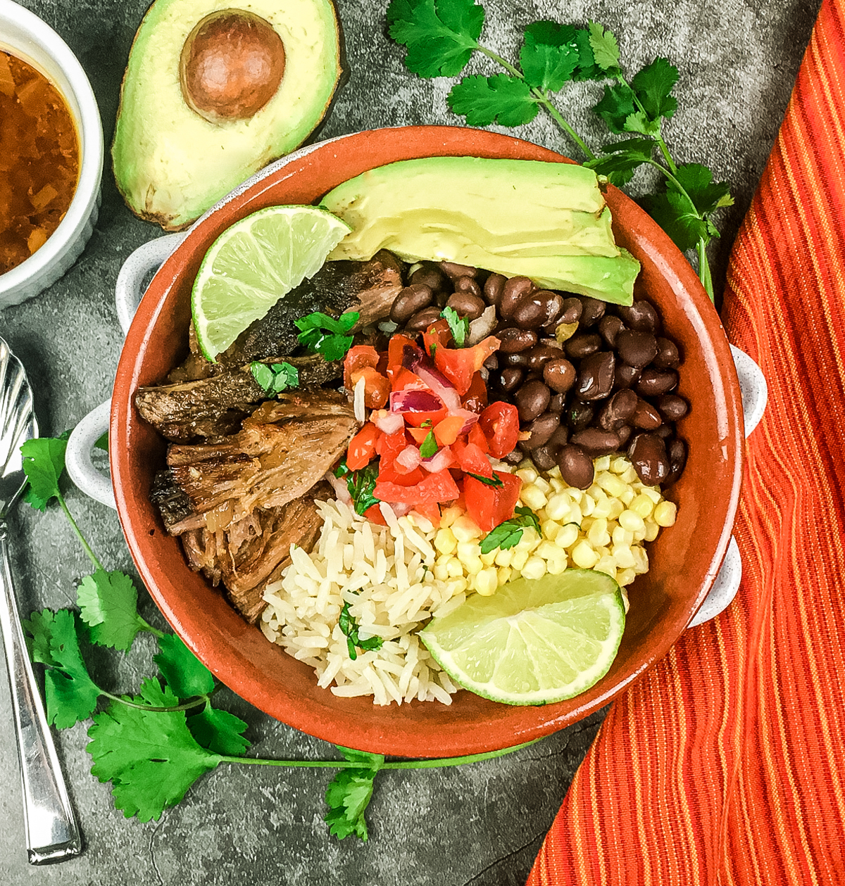 bowl filled with pork carnitas, rice, black beans, corn, avocado and salsa