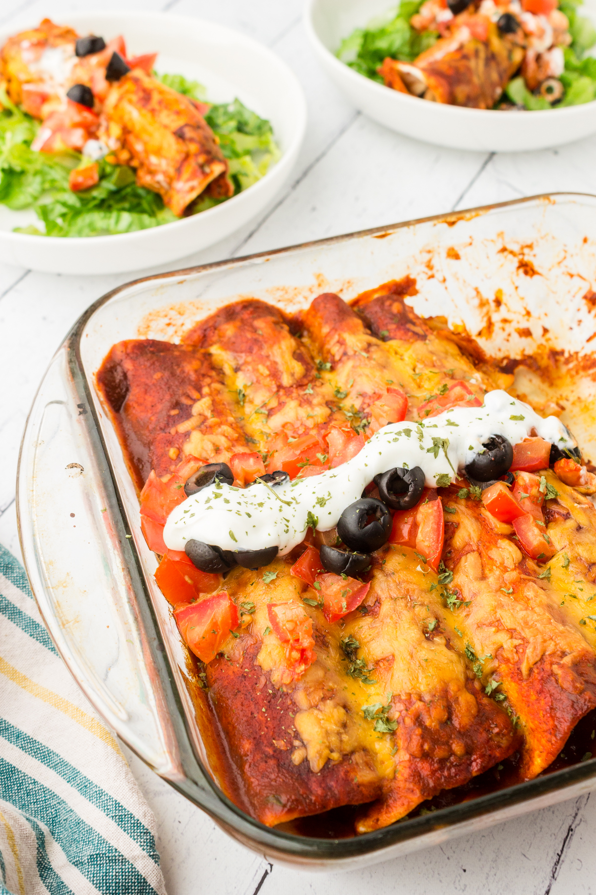 healthy chicken enchiladas served with salad greens and topped with diced tomatoes and sliced black olives