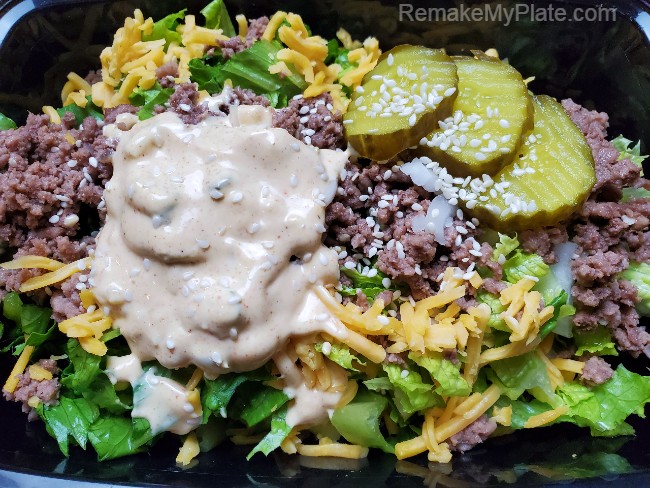take out container filled with keto Big Mac Salad topped with Copycat Big Mac Special Sauce