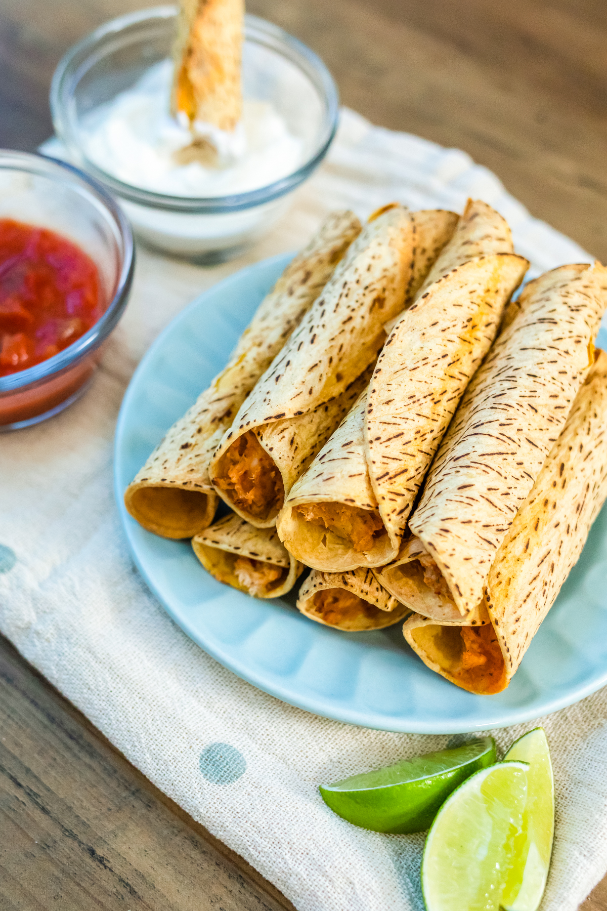 Chicken taquitos on a plate served with salsa and sour cream