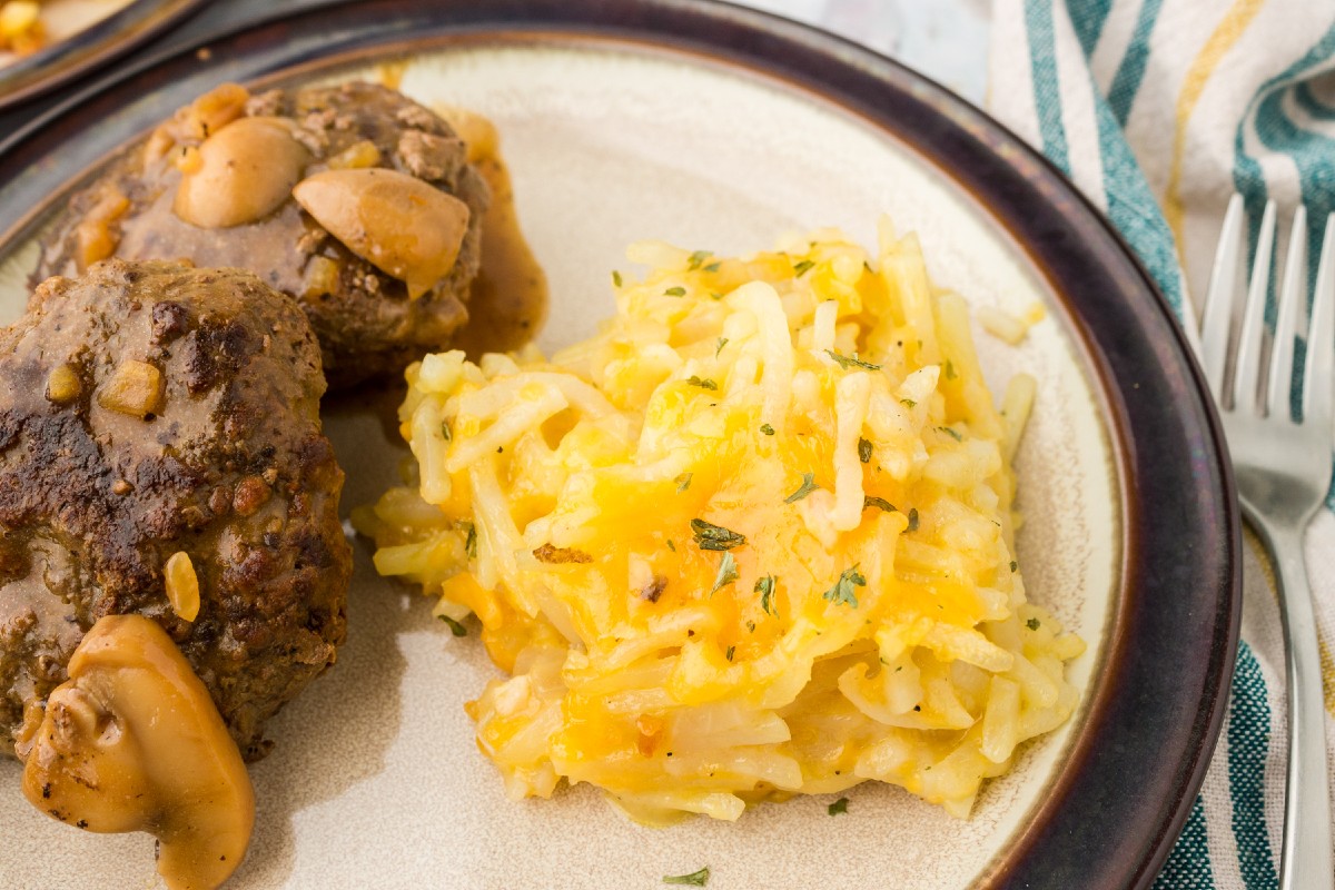 Easy Crockpot Hashbrown Casserole made Without Sour Cream on a plate being served with salisbury steaks