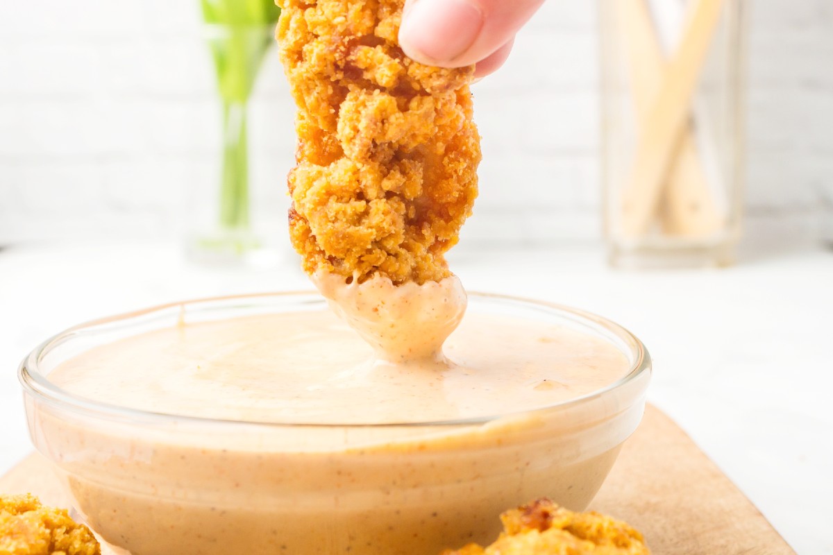 chicken tender being dipped into dipping sauce