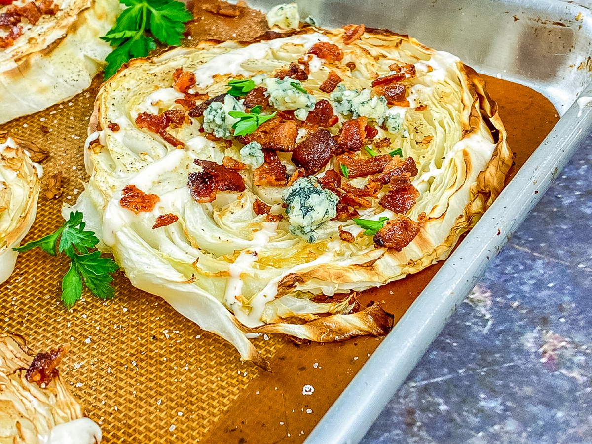 oven roasted cabbage steak on a baking pan sprinkled with bacon and blue cheese