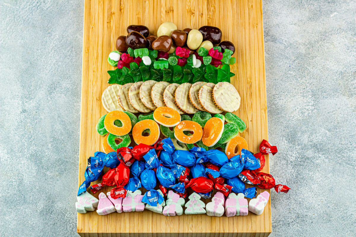 adding the cookies, gummy bears and stars and chocolate covered nuts on the dessert charcuterie board
