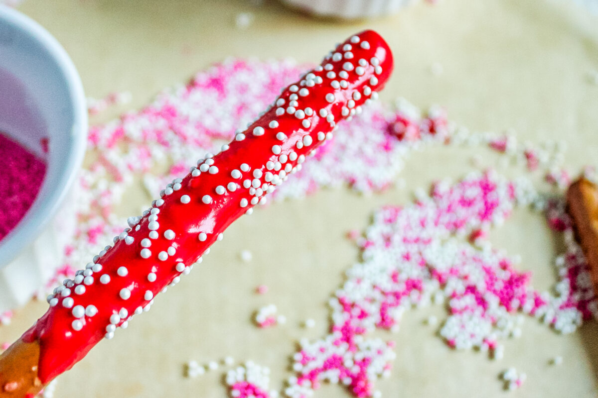 decorating the chocolate covered pretzel rods with sprinkles