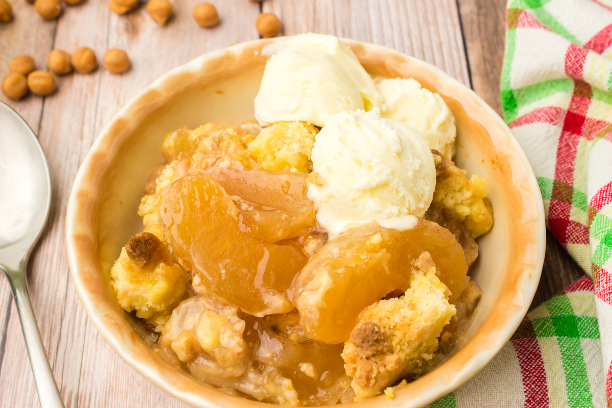 bowl full of caramel apple dump cake with whipped topping and a scoop of ice cream on the side