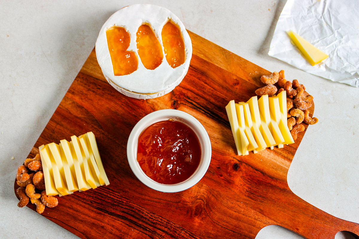 Adding the jar, brie, slices of cheese and nuts to the charcuterie board.