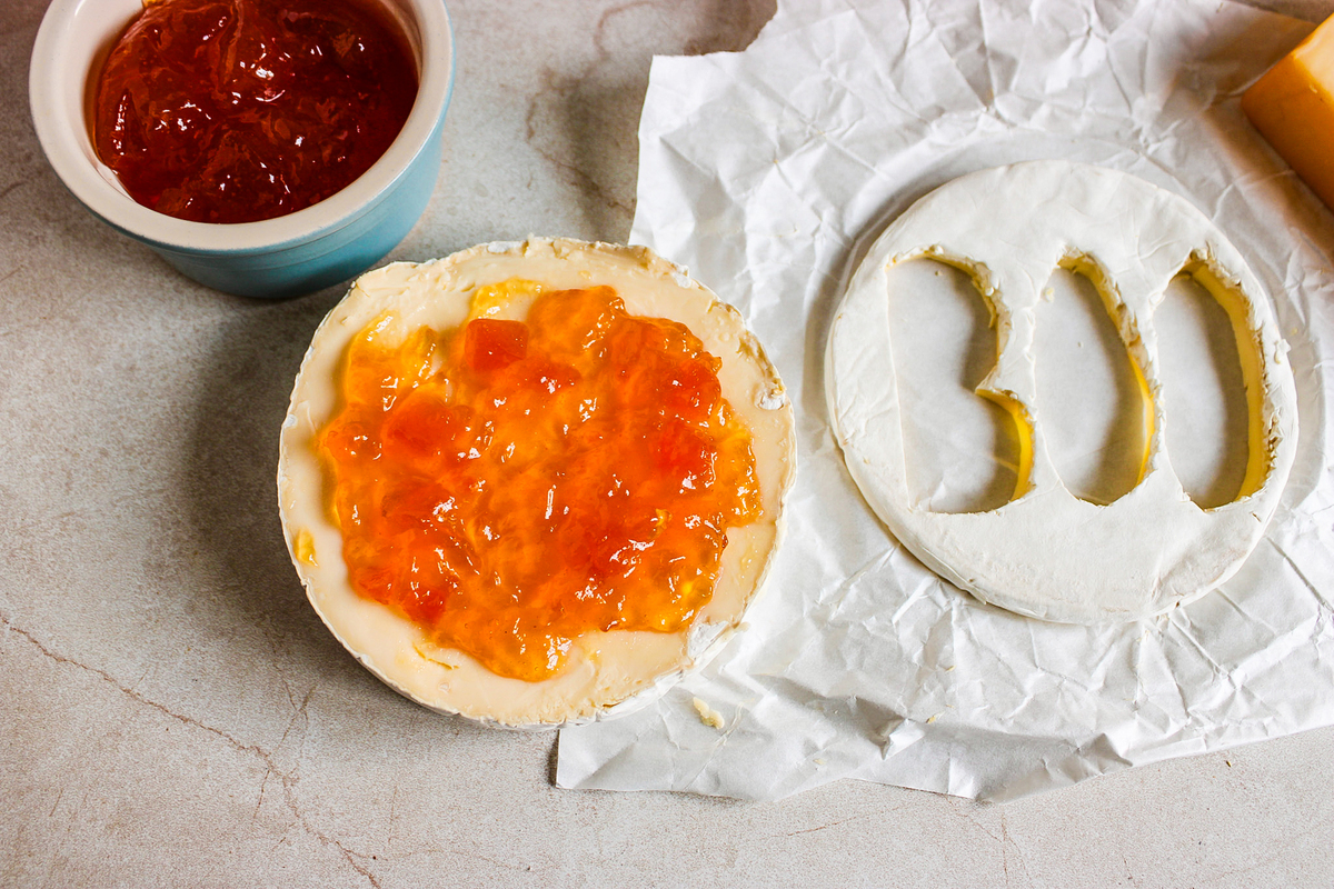 using a sharp knife to cut out the word BOO from the top of the round of brie cheese