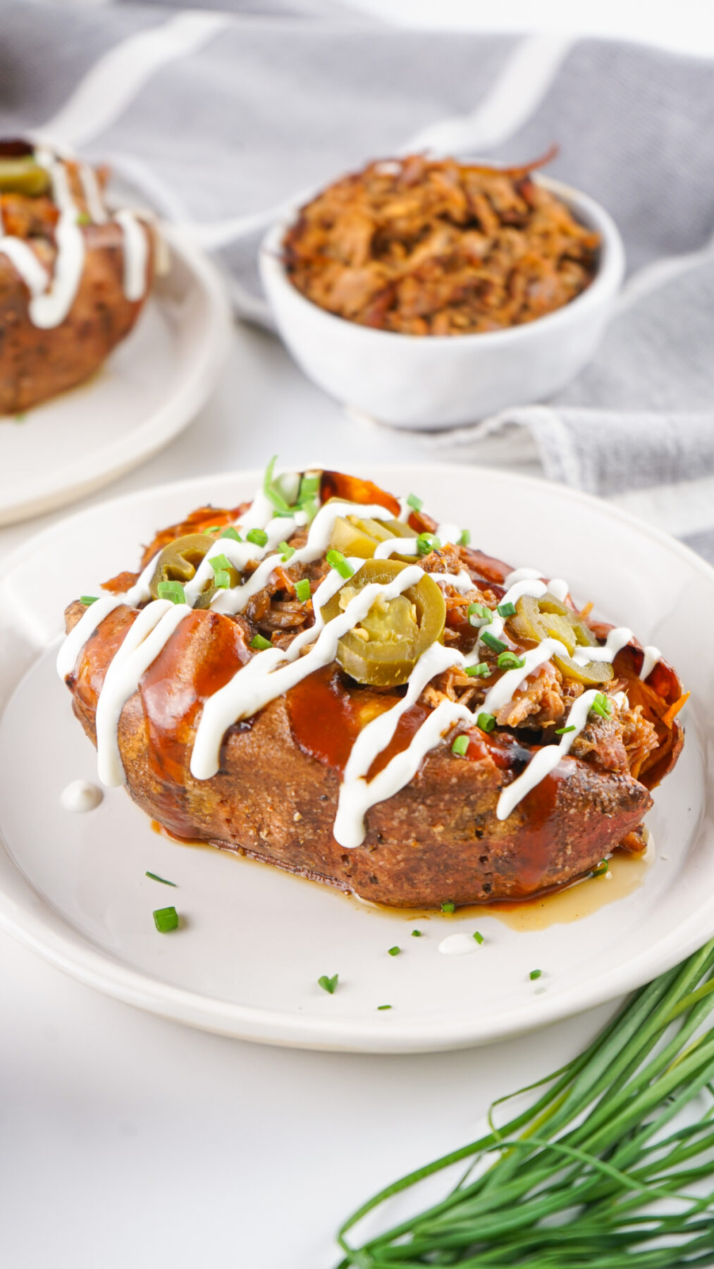 Pulled Pork Baked Sweet Potatoes topped with sour cream, jalapenos and chives on a plate.